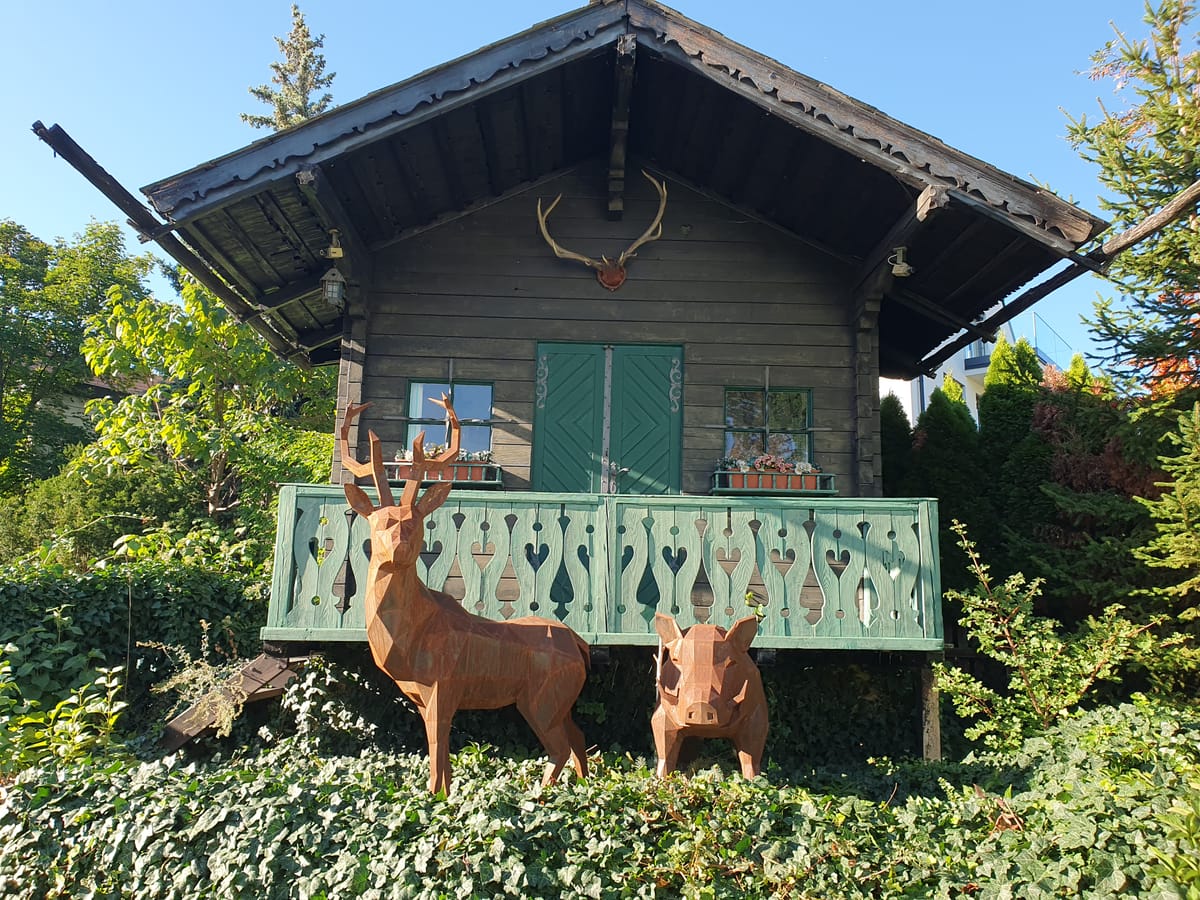 Hirsch und Wildschwein aus facettiertem Stahl vor einer Holzhütte im Garten